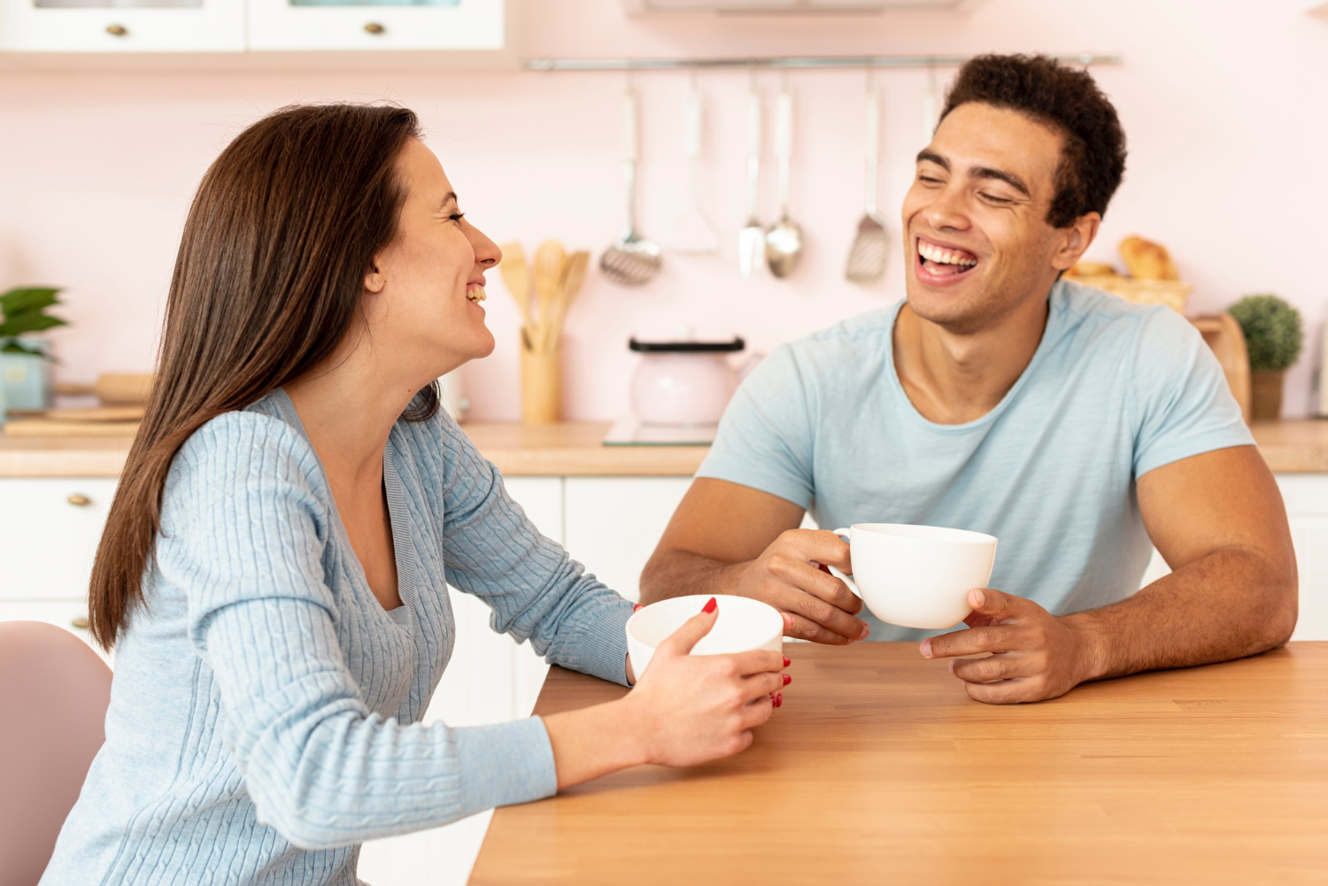 Couple laughing together at kitchen table with coffee